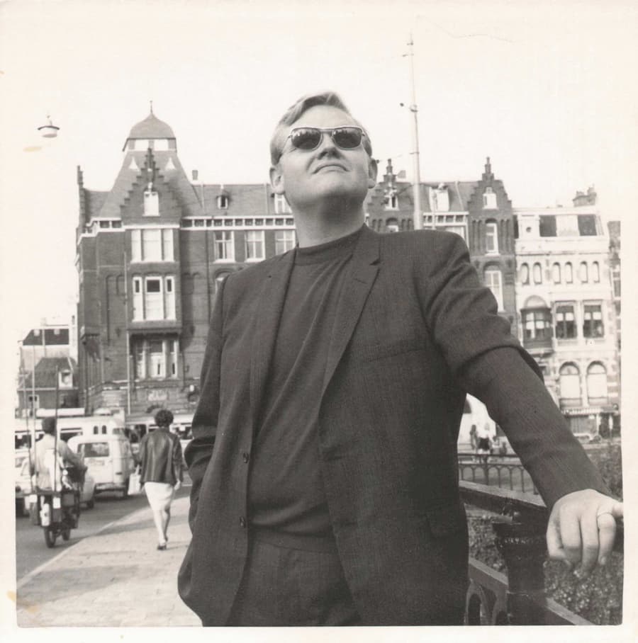 Frank Reynolds in sunglasses, leaning on a railing in a European city